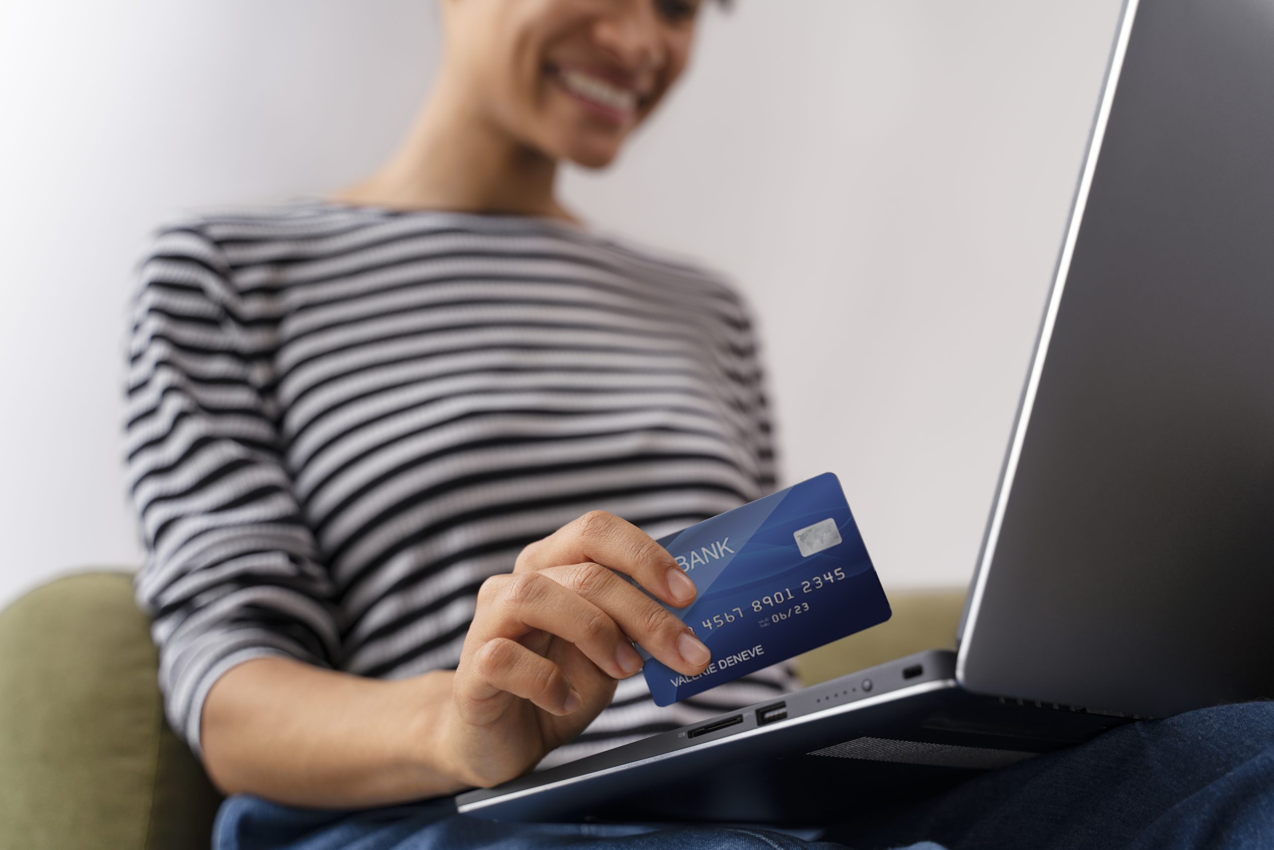 A person holding a payment card while sitting comfortably and using a laptop, illustrating the ease of making online transactions with payment cards.