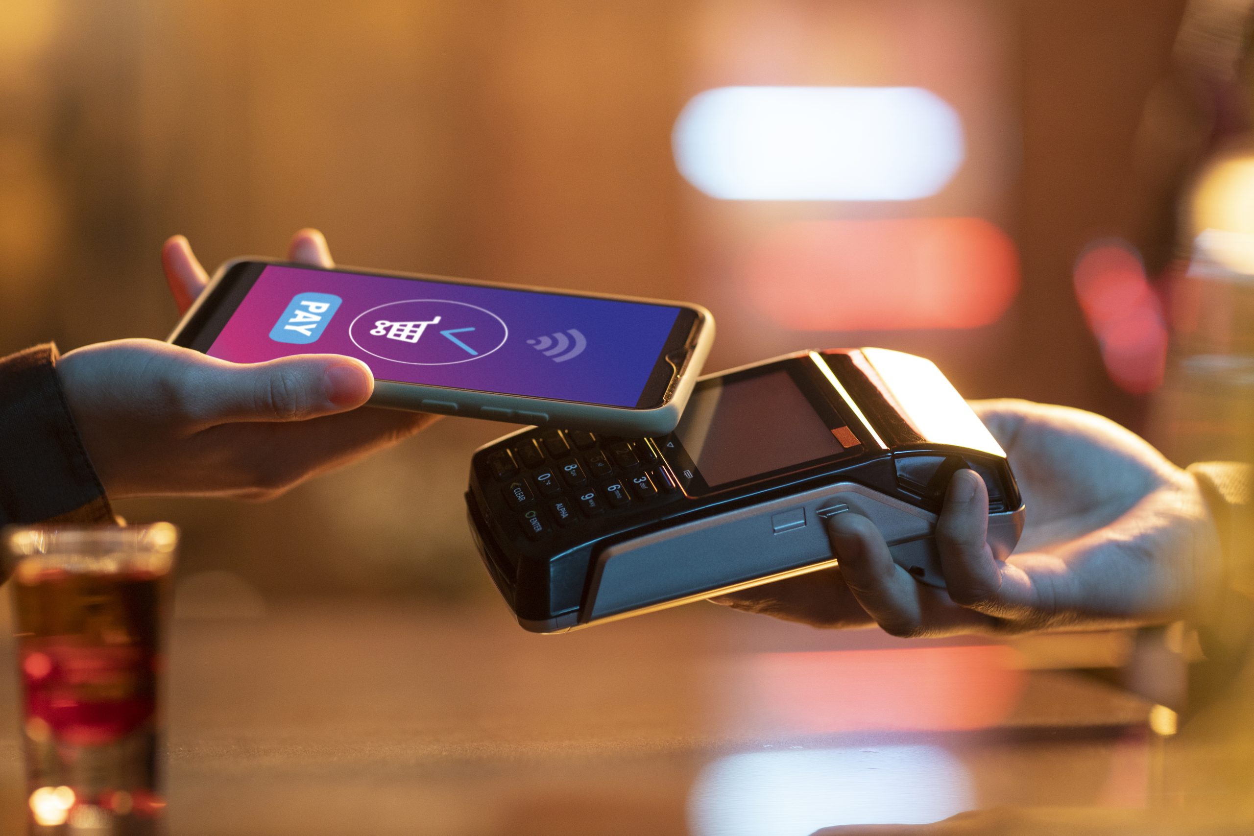 A person making a contactless payment using a smartphone over a card reader, highlighting the modern use of credit cards through mobile apps in a retail environment.