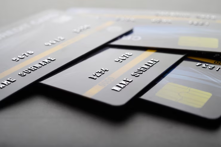 A close-up view of several metallic credit cards fanned out on a grey surface, highlighting the embossed numbers and names on their reflective surfaces.