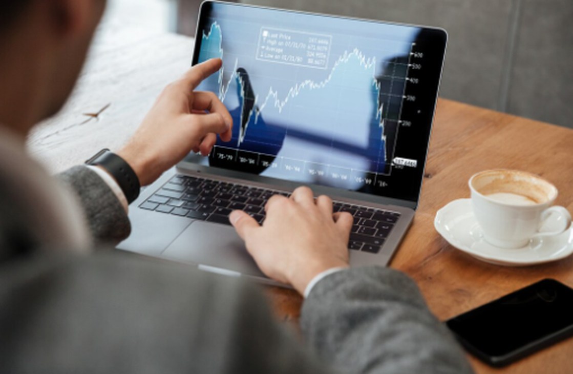 Businessman analysing financial charts on a laptop in a café, illustrating how global political volatility influences investment decisions and market performance.