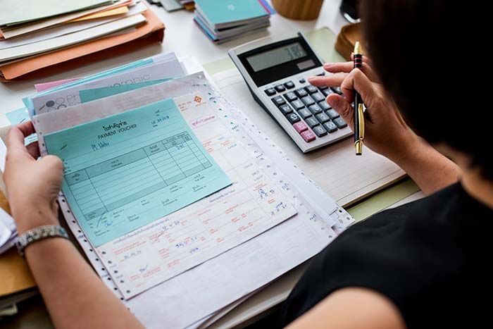 Person using a calculator and reviewing bills and receipts at a desk, illustrating the impact of rising living costs on household financial management.
