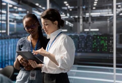 Two professionals discussing data on a tablet inside a modern server room, symbolising innovation, collaboration, and the growth of technology companies in the UK.